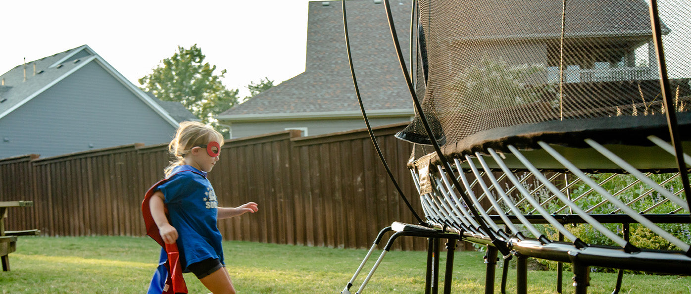 A photo of two kids playing with fall leaves with a SpringFree trampoline in their background.