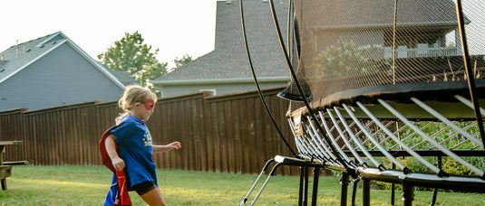 A photo of two kids playing with fall leaves with a SpringFree trampoline in their background.