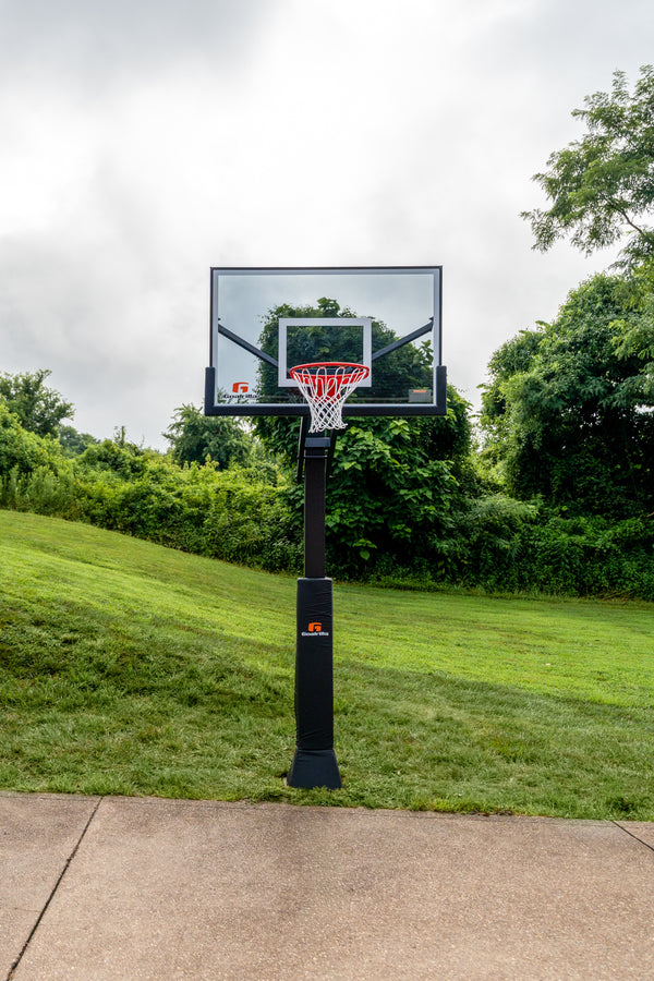 Load image into Gallery viewer, Basketball hoop on a grassy area with trees in the background
