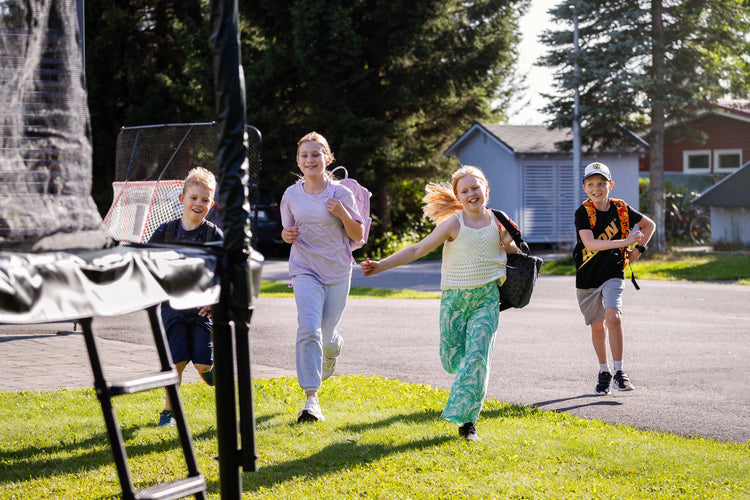Four children running towards a trampoline on a sunny day.