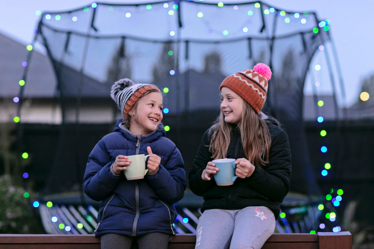 Two children sitting on a ledge holding mugs with colorful lights in the background.